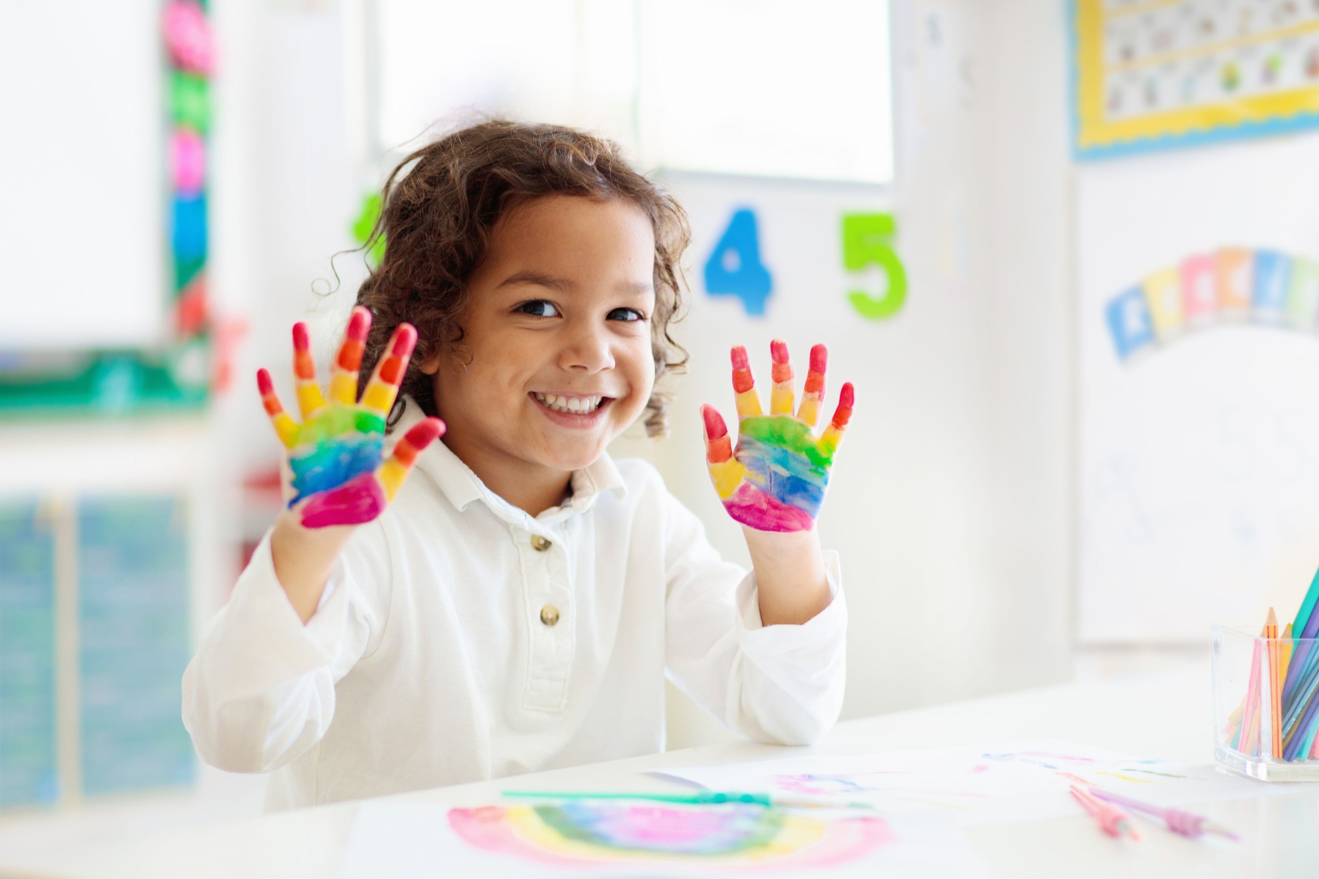 Child drawing rainbow. Paint on hands.